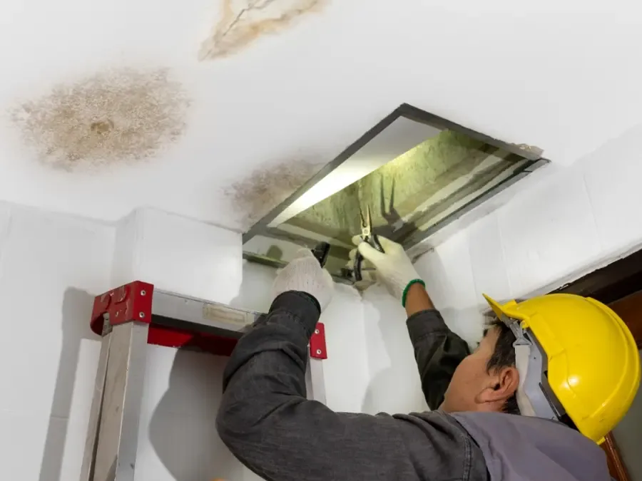 Worker inspecting a stained ceiling through an open hatch