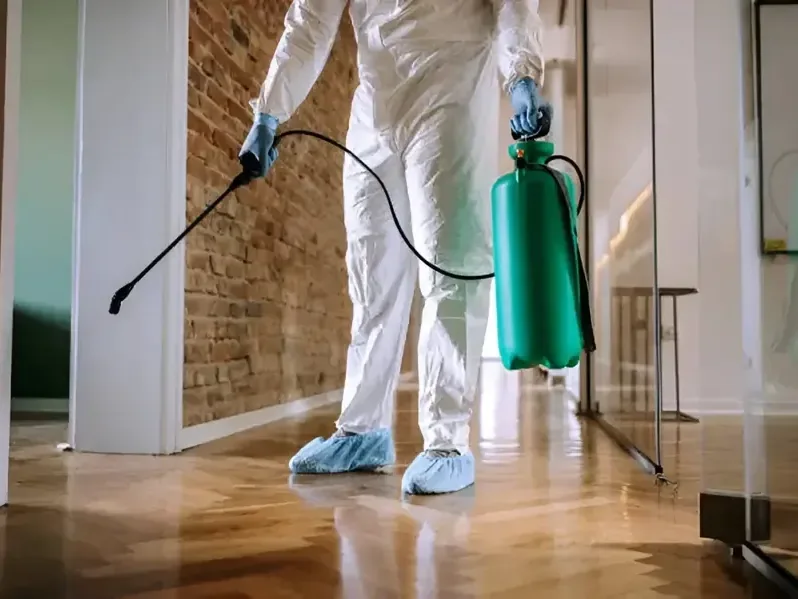 Worker in protective coveralls treating an indoor floor with a sprayer