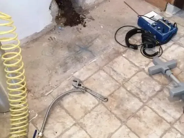 A drilled opening in a tile floor beside hoses and inspection equipment