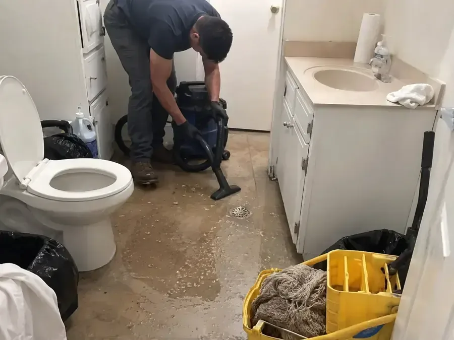 Technician using water removal equipment beside a toilet and vanity