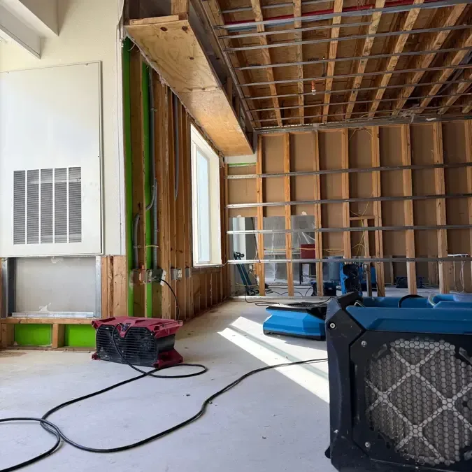 Technician removing wet drywall beside air movers and a dehumidifier